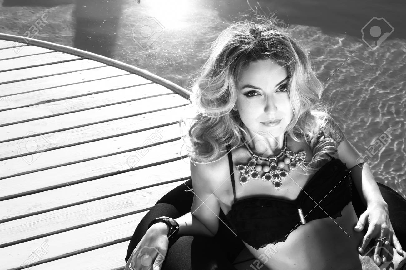 Black and white photo of beautiful sexy blonde woman laying near the swimming pool in black