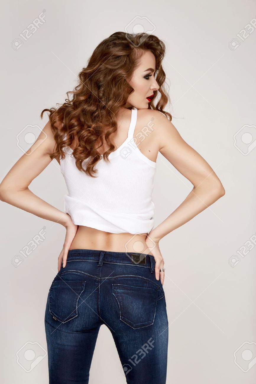 Beautiful young woman dressed in a black tight-fitting skinny denim jeans figure stands with his back to, brunette hair, make-up hair, red lipstick, clothing - 51002754 Beautiful young woman dressed in a black tight-fitting skinny denim jeans figure stands with his back to, brunette hair, make-up hair, red lipstick, clothing - 51002754