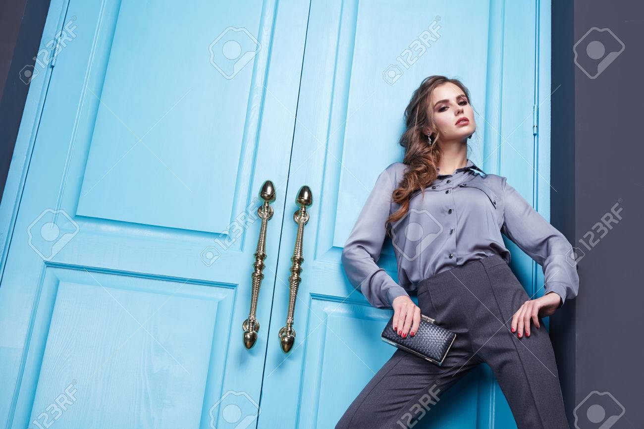 美しいセクシーな女の子は ファッション衣料品コレクション モダンでスタイリッシュなパンツ ハイヒールで派手なシルクのシャツ アクセサリー靴 青いドア入口出口室内空間の新しいカタログのスタイルを服を着せた の写真素材 画像素材 Image