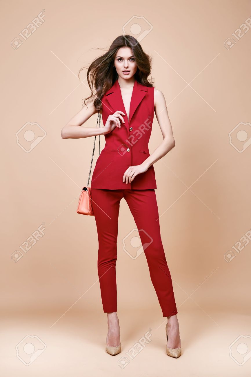 Beautiful brunette woman wear red silk costume jacket and pants summer collection clothes for business lady casual work office style hold small lather goods bag make a pose fashion model catalog. - 54632974 Beautiful brunette woman wear red silk costume jacket and pants summer collection clothes for business lady casual work office style hold small lather goods bag make a pose fashion model catalog. - 54632974