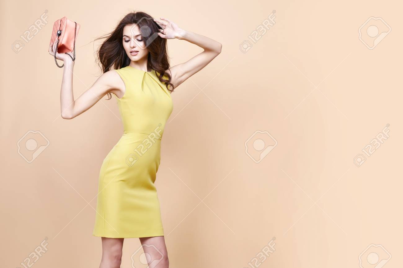 Glamour fashion woman long brunette curly hair natural evening makeup wear short stylish yellow cotton dress from new catalog spring summer collection accessory handbag jewelry body shape care. - 54633067 Glamour fashion woman long brunette curly hair natural evening makeup wear short stylish yellow cotton dress from new catalog spring summer collection accessory handbag jewelry body shape care. - 54633067