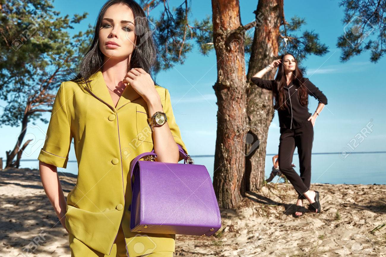 セクシーな美しい女性の砂浜ビーチは池海岸ビーチ バケーション リゾート ファッション スタイル 2 つブルネット衣装メイクを歩行アクセサリー バッグ トレンド友人パンツとブラウス夏コレクションの松林します の写真素材 画像素材 Image