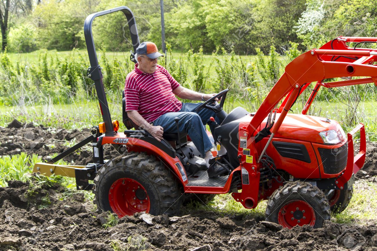 Elderly Man Plowing His Garden With A Compact 4x4 Tractor Stock