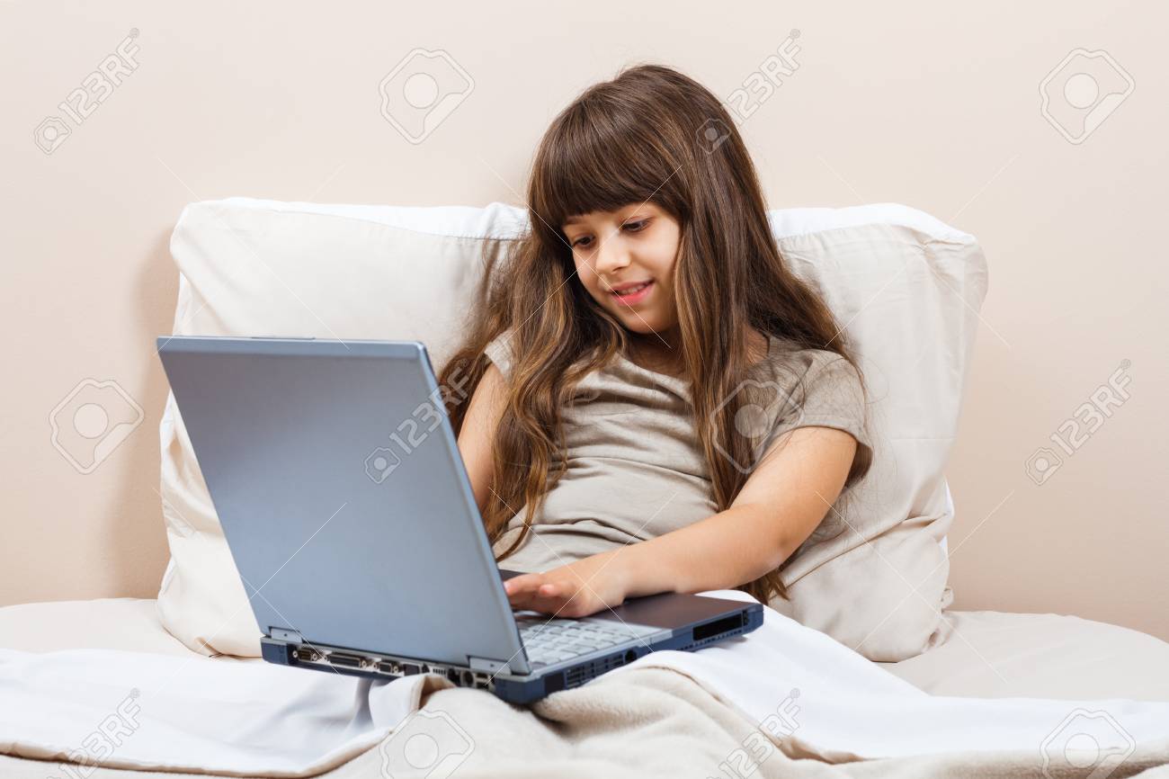 パジャマでかわいい女の子が彼女のベッドに座っているとラップトップを使用しています の写真素材 画像素材 Image