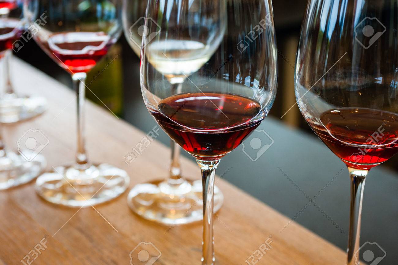 Detail of wine glasses with red wine samples, on wood counter with other glasses in background. - 52146861 Detail of wine glasses with red wine samples, on wood counter with other glasses in background. - 52146861