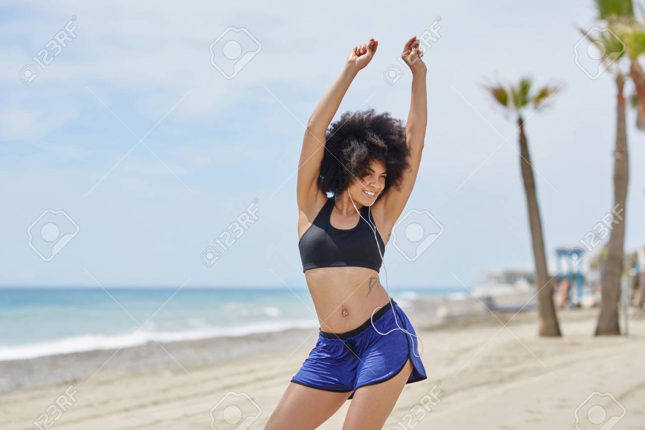 happy afro american woman listening music and dancing on beach stock
