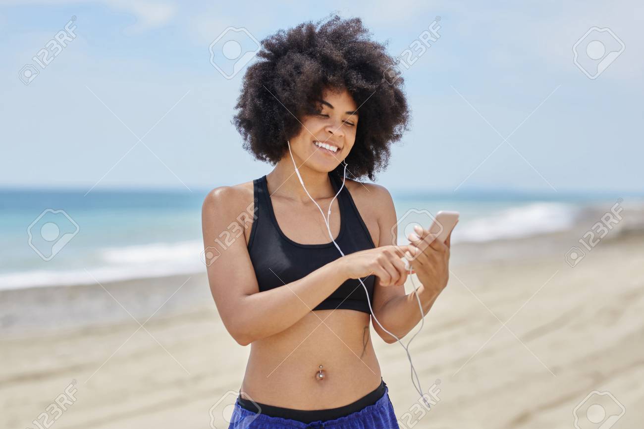 happy afro american woman on beach listening music on mobile stock