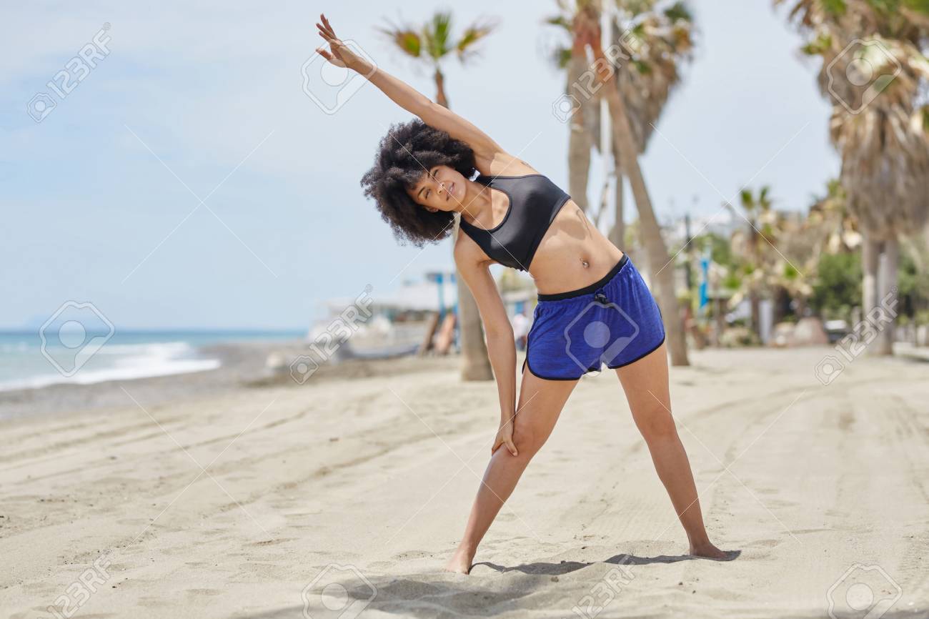 happy afro american sportswoman stretching body on beach stock photo