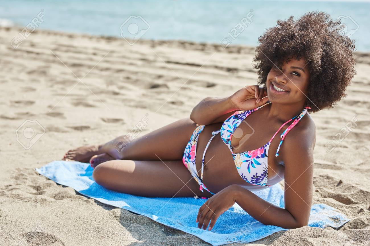 happy afro american woman lying on beach with hand on neck stock