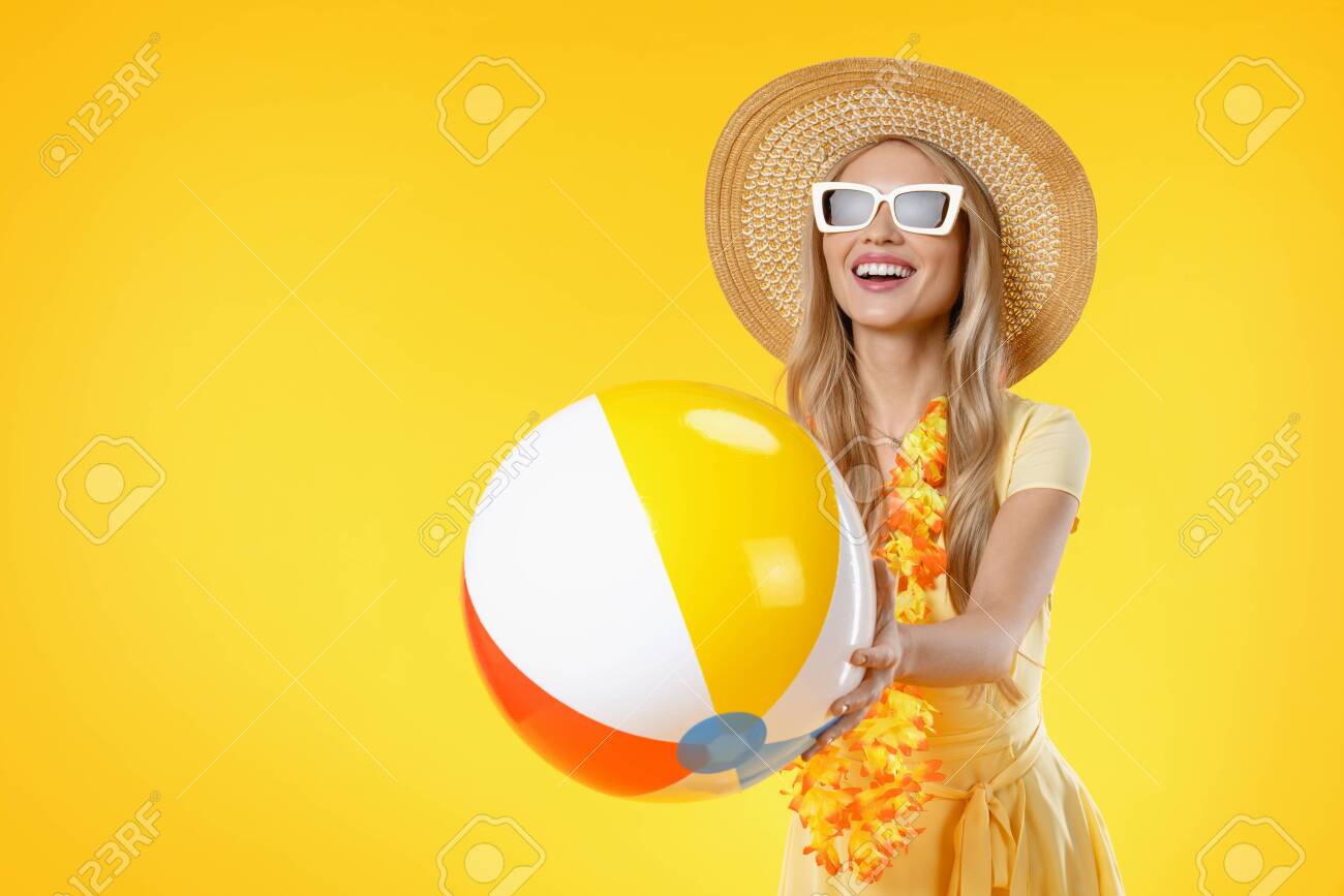 Attractive woman with beach accessories holding colorful ball on yellow background - 138582698 Attractive woman with beach accessories holding colorful ball on yellow background - 138582698