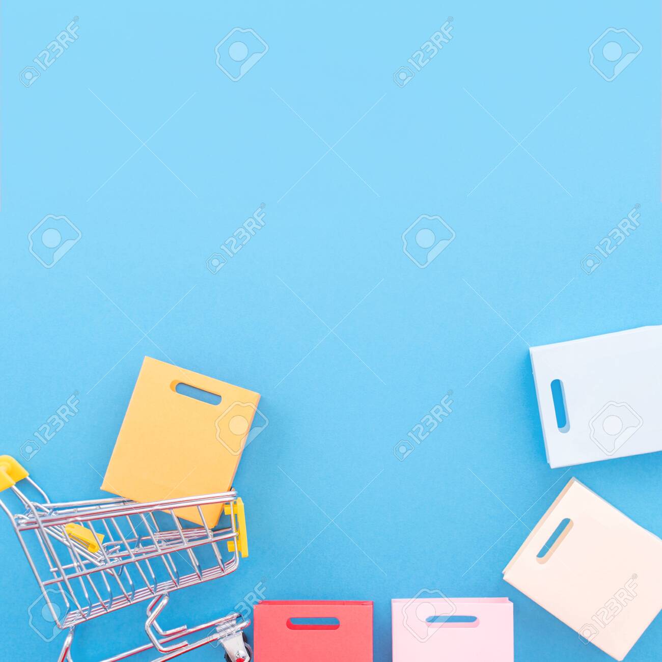Abstract design element, annual sale, shopping season concept, mini yellow cart with colorful paper bag on pastel blue background, top view, flat lay - 131009060 Abstract design element, annual sale, shopping season concept, mini yellow cart with colorful paper bag on pastel blue background, top view, flat lay - 131009060