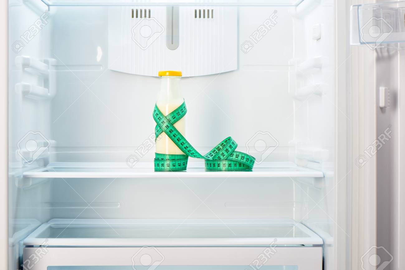 Kühlschrank Regal : Glasflasche von joghurt mit maßband auf dem regal der offenen leeren Kühlschrank Regal : Glasflasche von joghurt mit maßband auf dem regal der offenen leeren