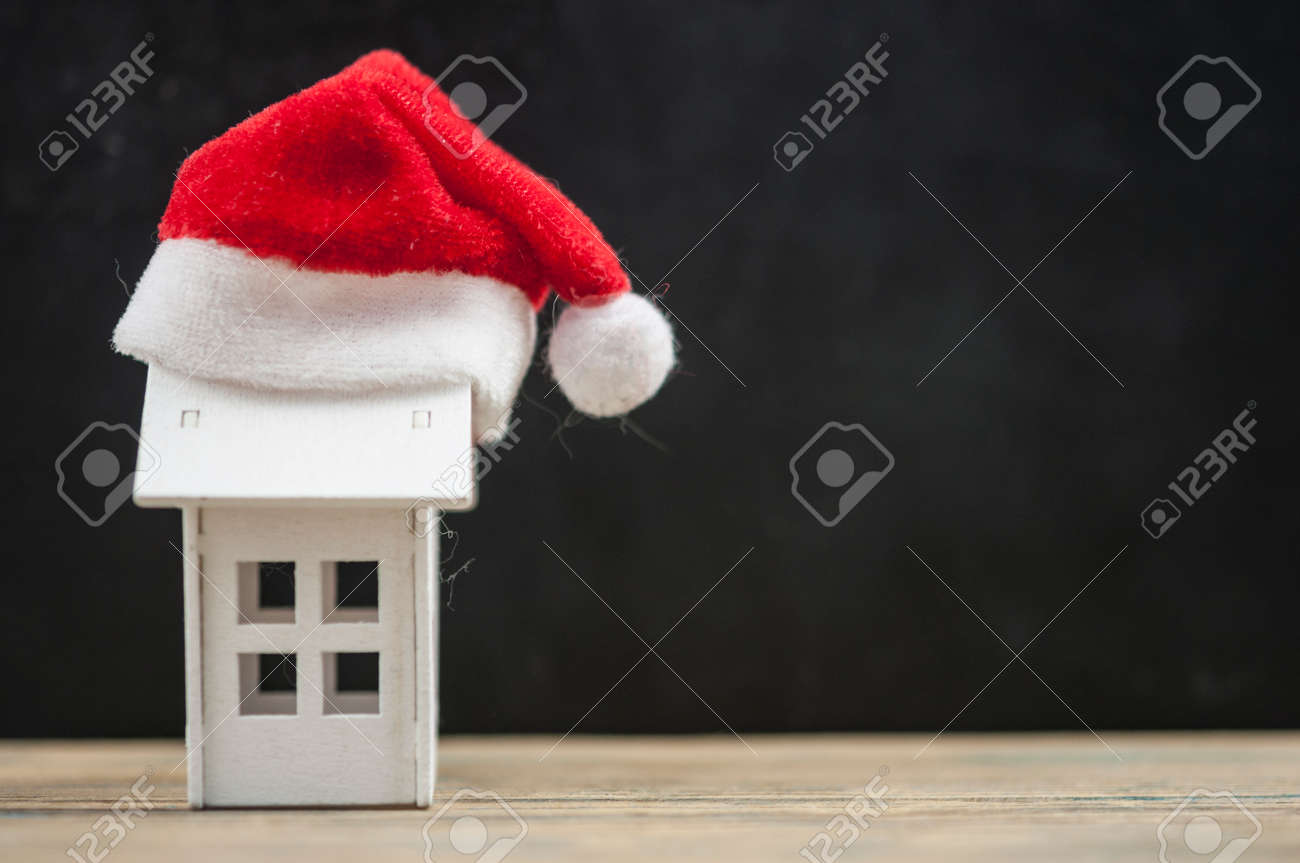 Santa hat with miniature house model on wooden table - 157979865 Santa hat with miniature house model on wooden table - 157979865