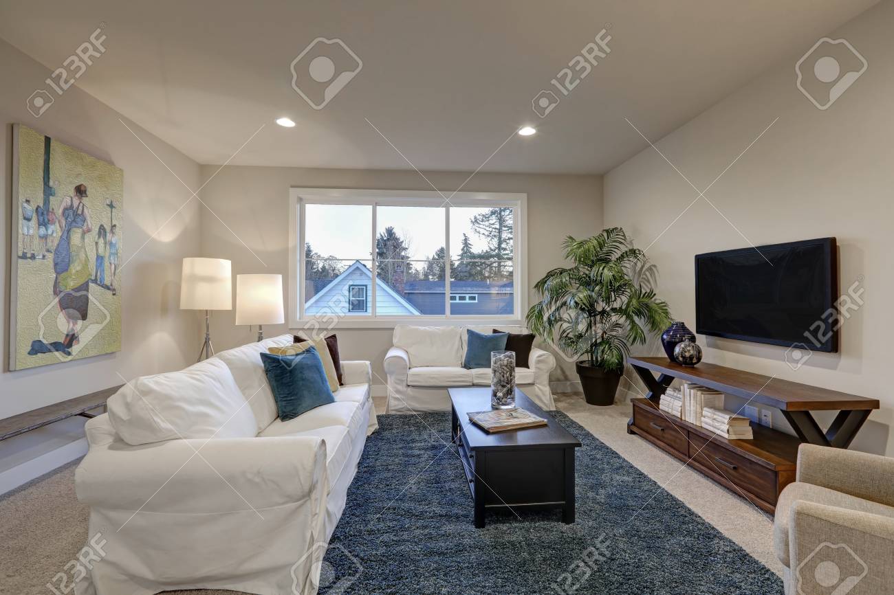 White And Beige Living Room With Blue Accent Rug Atop Beige Carpet Stock Photo