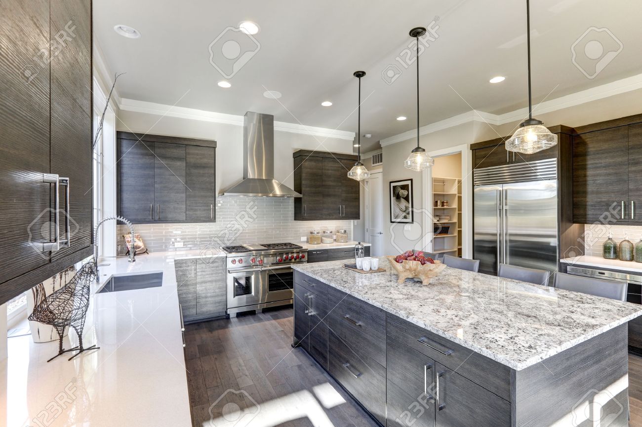 Modern gray kitchen features dark gray flat front cabinets paired with white quartz countertops and a glossy gray linear tile backsplash. Bar style kitchen island with granite counter. Northwest, USA - 70177674 Modern gray kitchen features dark gray flat front cabinets paired with white quartz countertops and a glossy gray linear tile backsplash. Bar style kitchen island with granite counter. Northwest, USA - 70177674