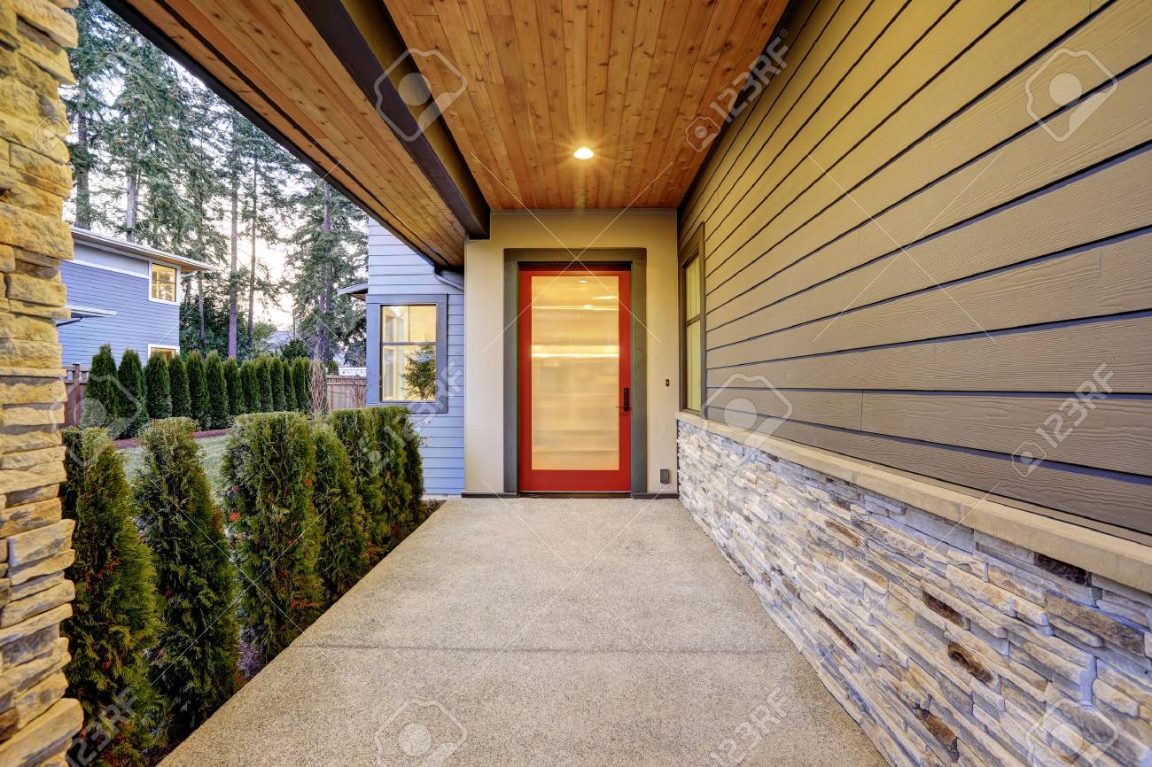 Entrance of Luxurious new construction home with long covered porch that features plank ceiling, natural stone wall design and modern glossy front door. Northwest, USA - 70296421 Entrance of Luxurious new construction home with long covered porch that features plank ceiling, natural stone wall design and modern glossy front door. Northwest, USA - 70296421