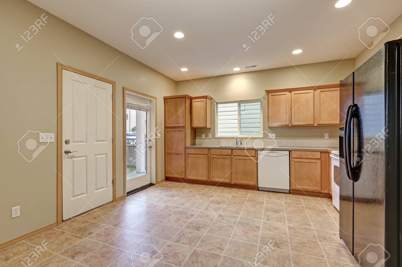 Sala De Cocina Luminosa Y Aireada Con Paredes Recién Pintadas En Color Beige Gabinetes De Madera Clara Y Refrigerador Negro Sobre Piso De Baldosas