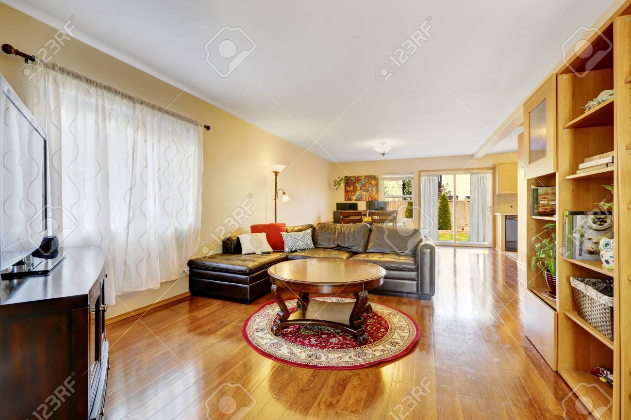 Open Floor Living Room With Warm Yellow Walls, Wood Laminate Flooring,  Furnished With Grey Leather Sectional, Built In Bookcase With Open Shelves  And Round Coffee Table. Northwest, USA Stock Photo, Picture and, image size:1300x866