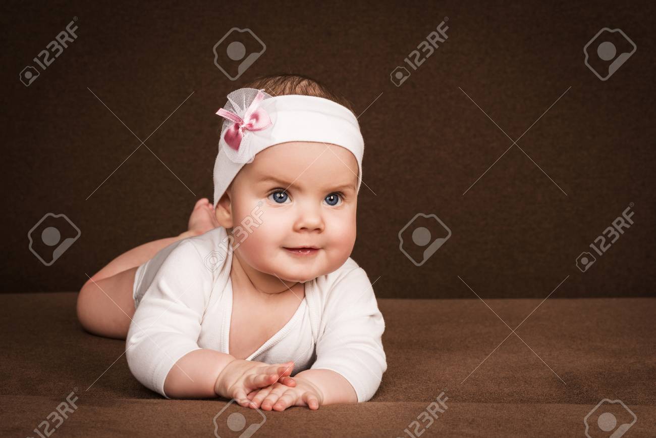 Mignonne Petite Fille Avec Une Fleur D Arc Sur La Tete Enfant Aux Grands Yeux Bleus Se Trouve Sur Son Ventre Sur Un Canape Marron Sur Fond Marron Banque D Images Et Photos Libres