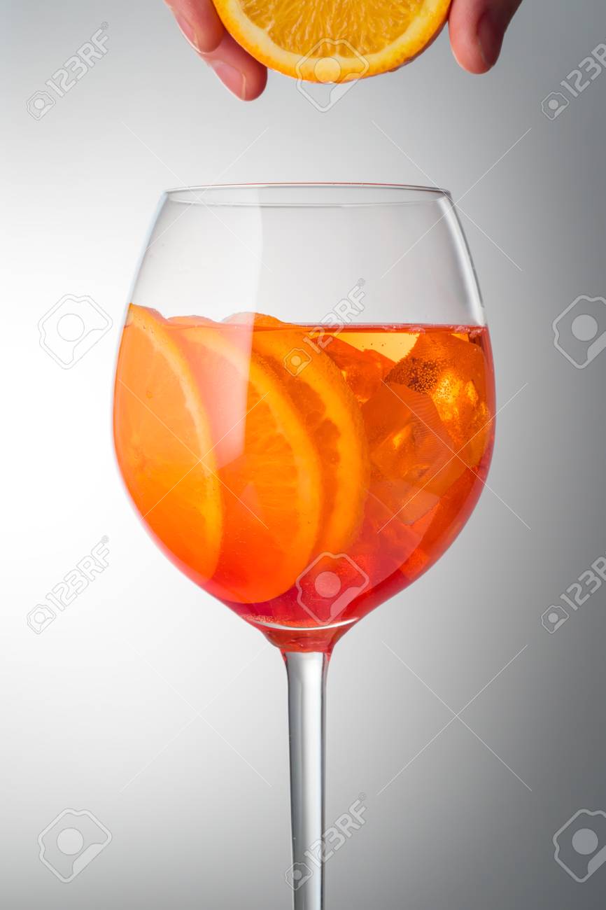 トレンディな人気イタリアドリンク夏爽やかなかすかにアルコールカクテルアペロールスプリッツは ホワイトグレーの光拡散グラデーションの背景にオレンジ色のスライスで飾られた氷でガラスグラスで新鮮なオレンジジュースの模倣ドロップ の写真素材 画像素材 Image