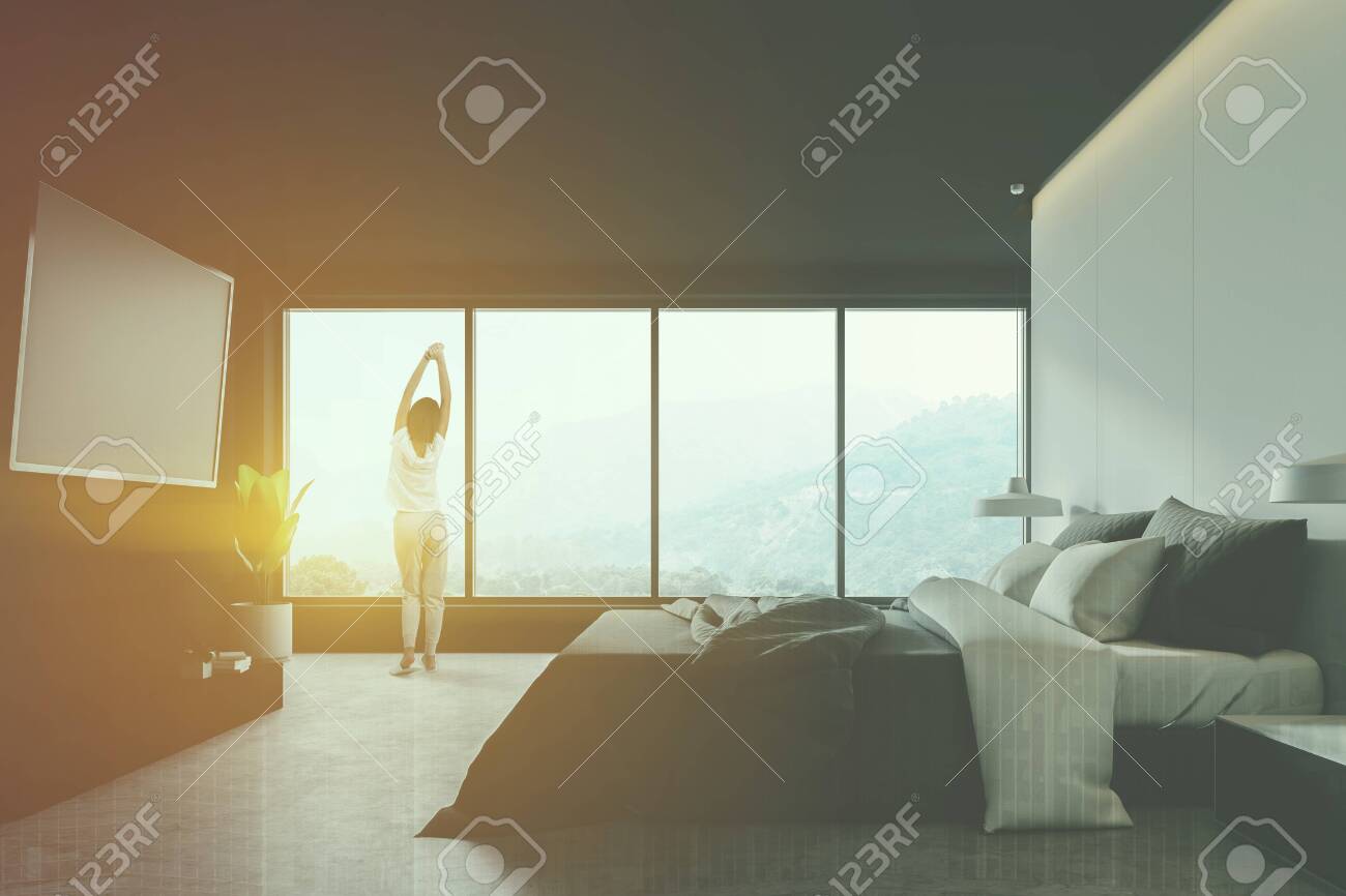 Woman In Pajamas Standing In Modern Bedroom Interior With White