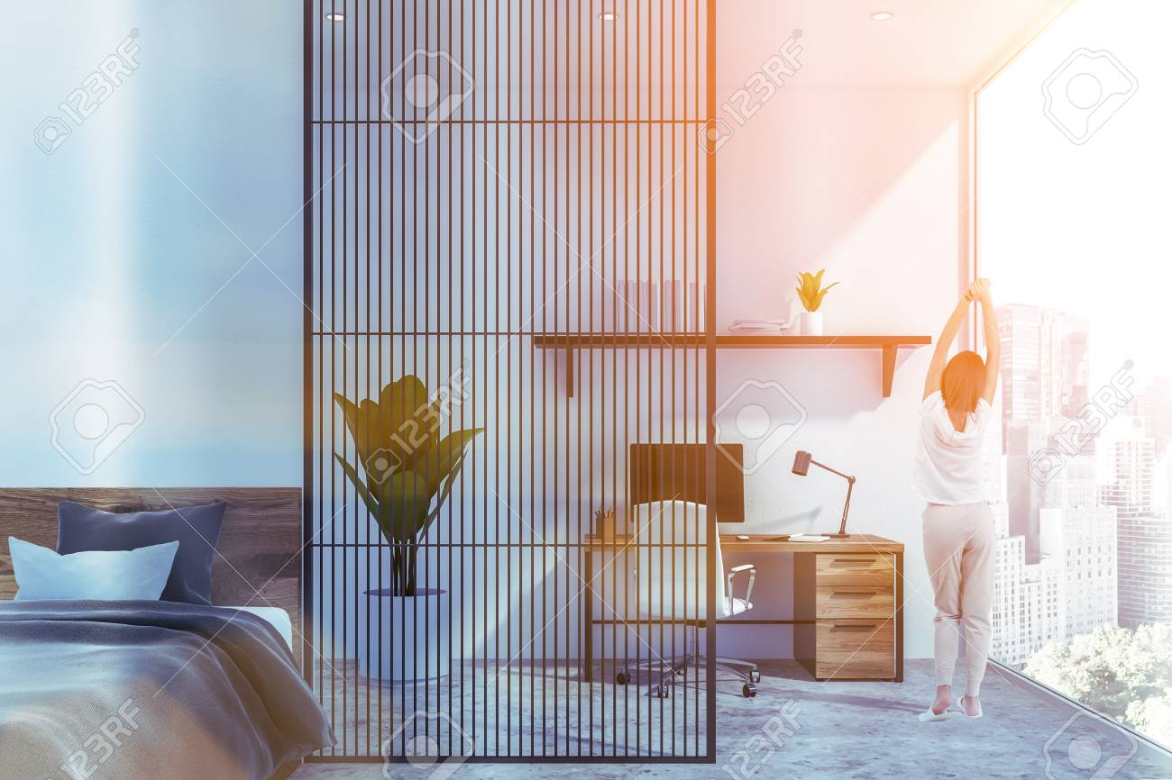 Young Woman Standing In Modern White Bedroom With Comfortable