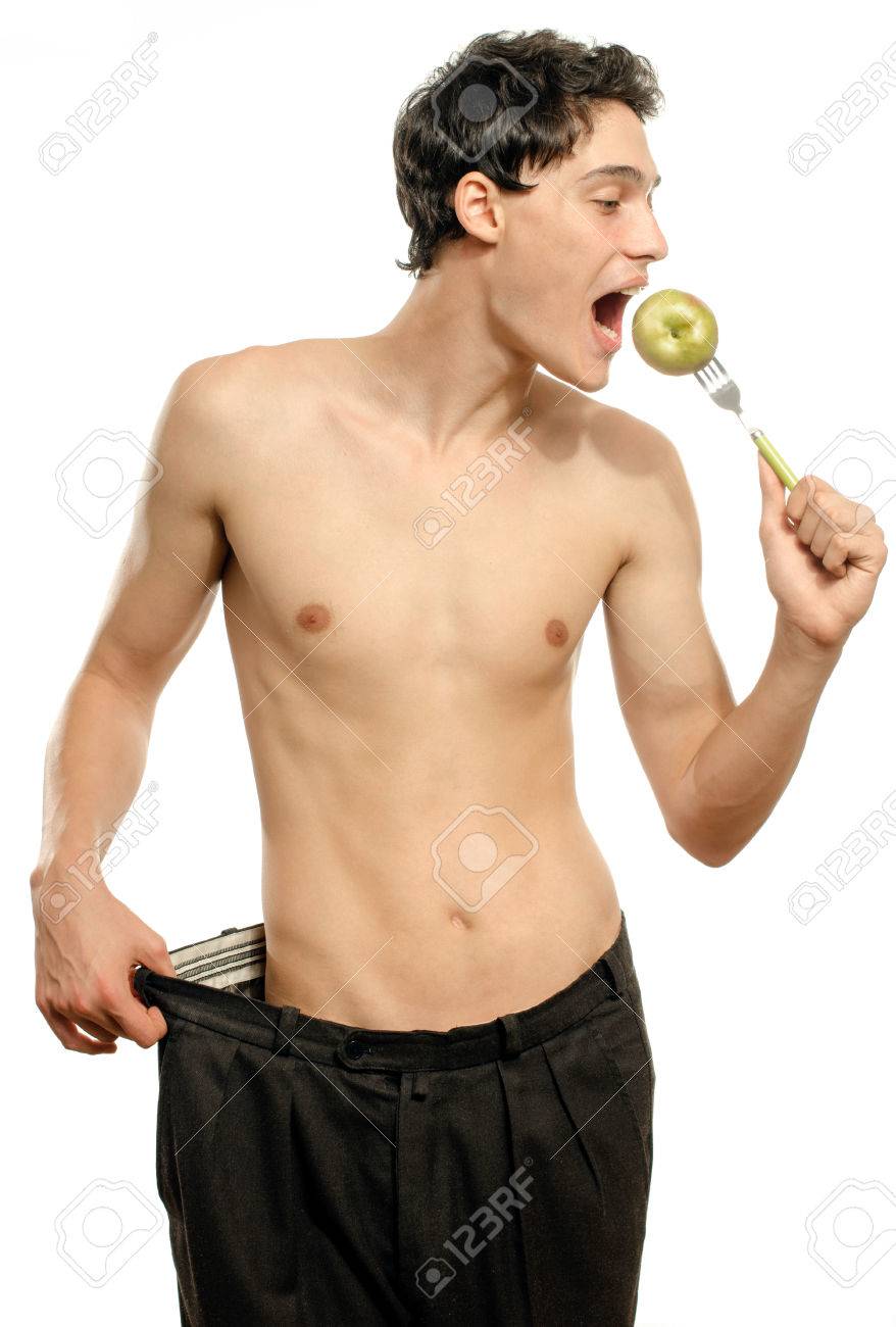 リンゴ 拒食症を食べる大型のズボンと痩せた若い男は スリムなボディを見てください 男は体重を失い 脂肪だった時代から大きなズボンを比較します 前に と後に 脂肪やスリム の写真素材 画像素材 Image