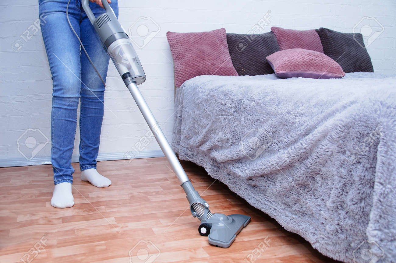 Handheld gray vacuum cleaner in the hand of a Caucasian woman in jeans. Vacuum the floor in the room. - 166396150 Handheld gray vacuum cleaner in the hand of a Caucasian woman in jeans. Vacuum the floor in the room. - 166396150