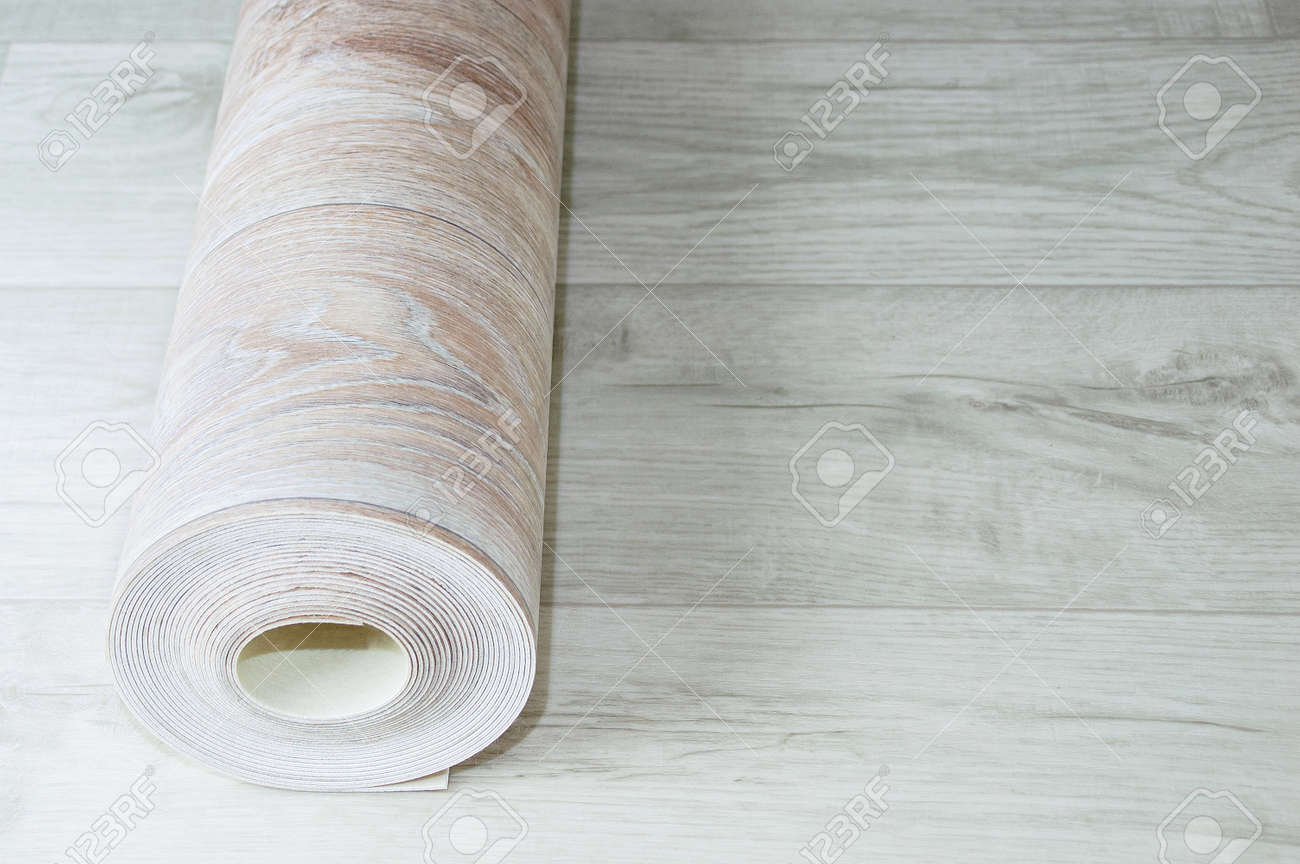 Rolled up roll of beige linoleum with wood texture on white wood floor. Home renovation and improvement. - 170078428 Rolled up roll of beige linoleum with wood texture on white wood floor. Home renovation and improvement. - 170078428