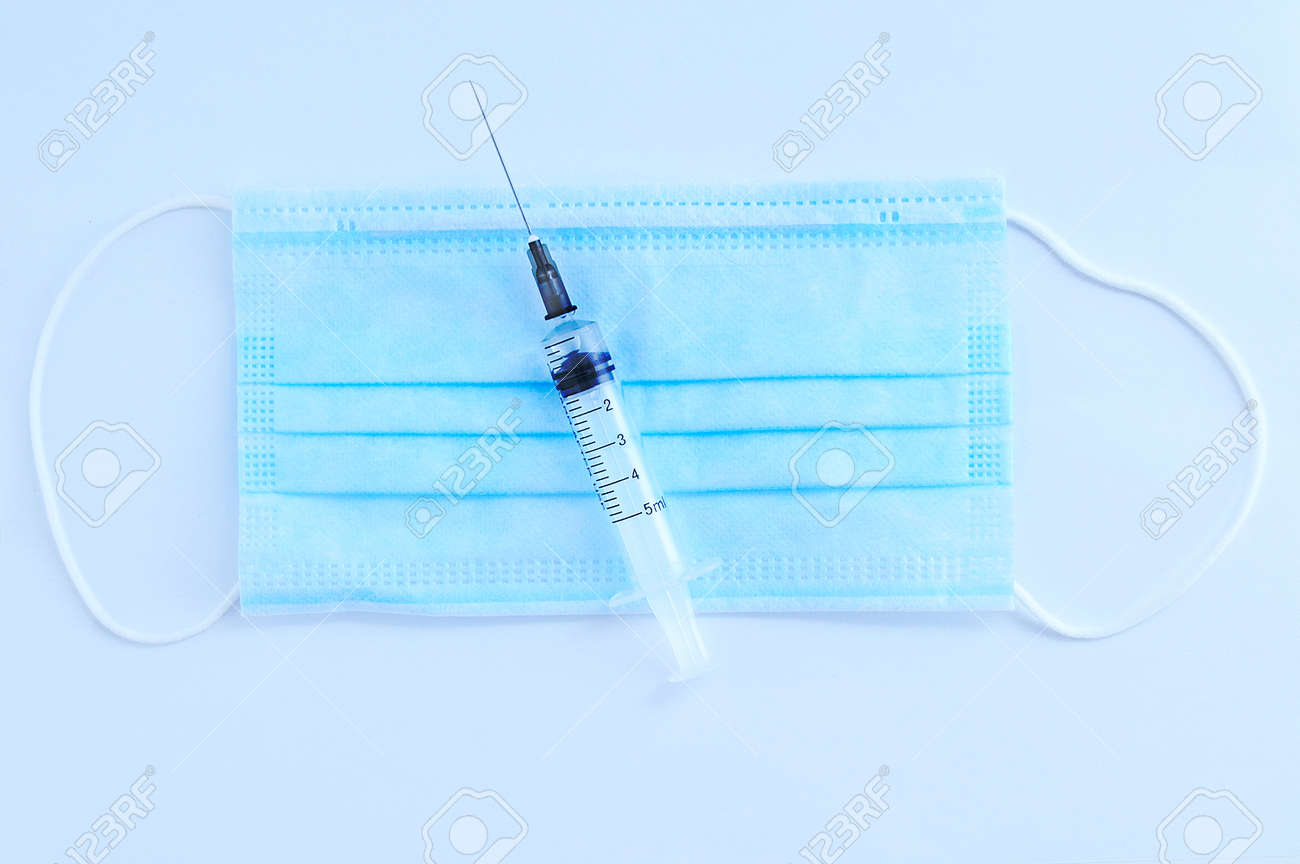 Blue medical protective mask and syringe with a needle. White background. View from above. - 171610482 Blue medical protective mask and syringe with a needle. White background. View from above. - 171610482