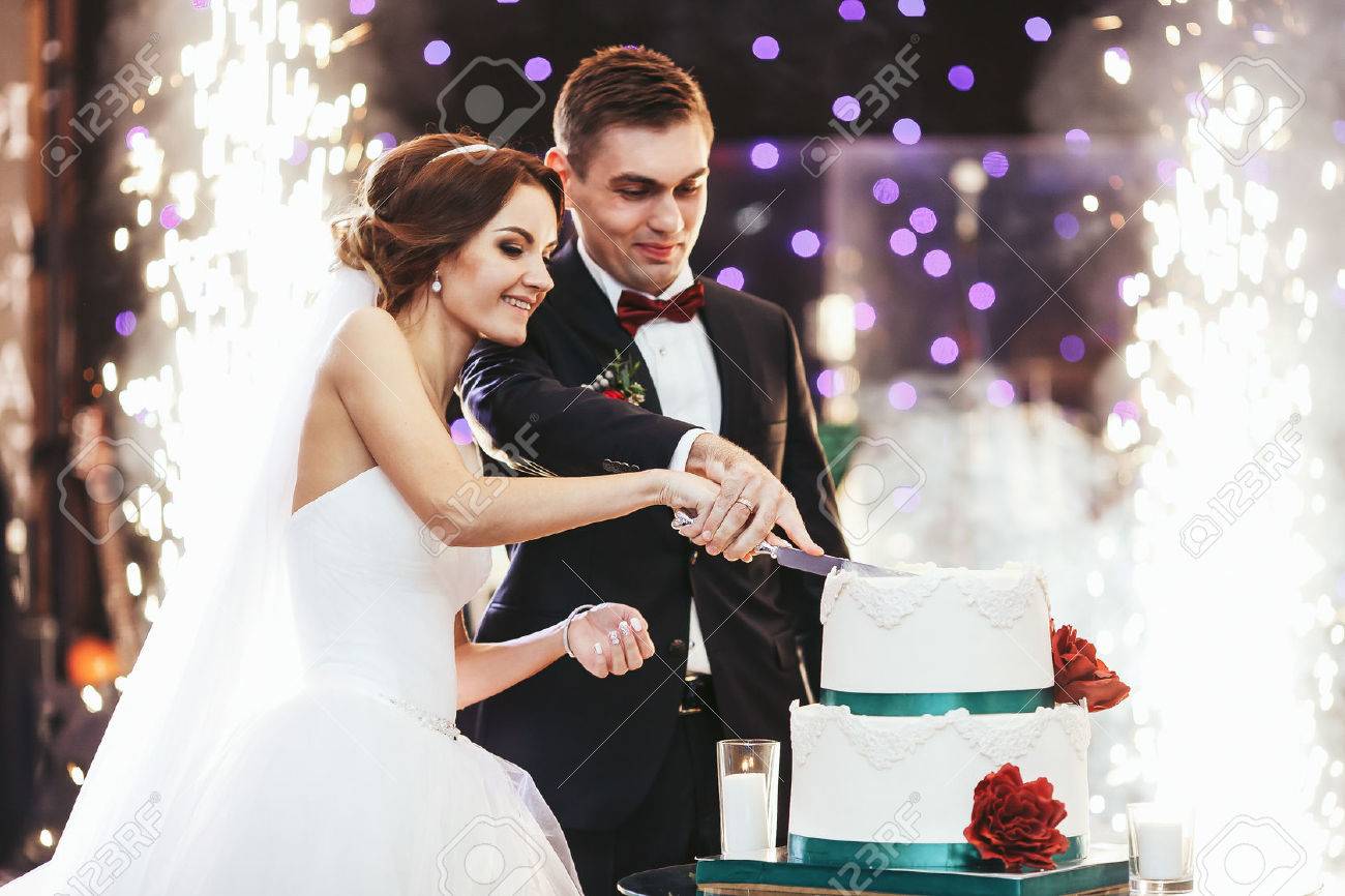 Happy bride and groom cut the wedding cake in the front of fireworks - 64223820 Happy bride and groom cut the wedding cake in the front of fireworks - 64223820