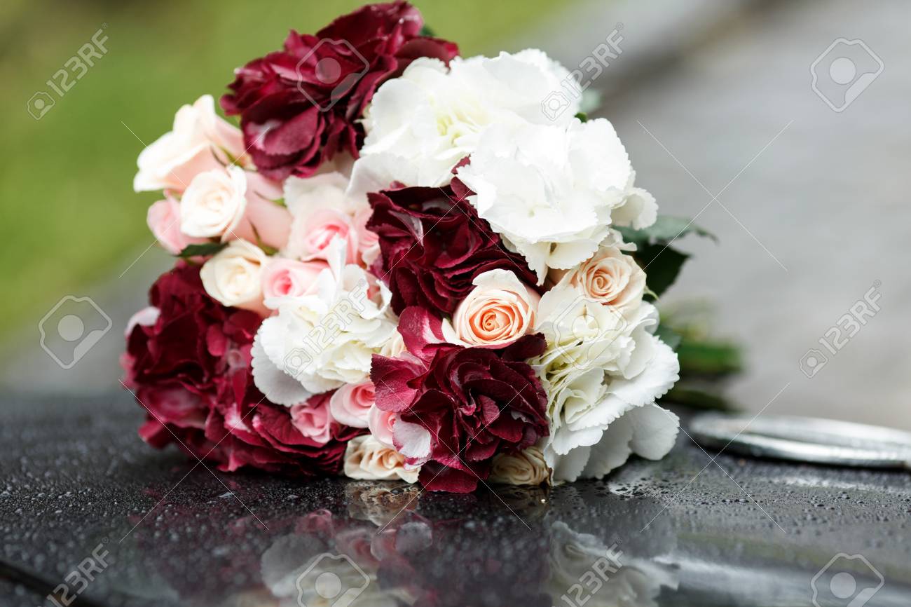 bouquet of wine colored and white flowers lies on a black car stock