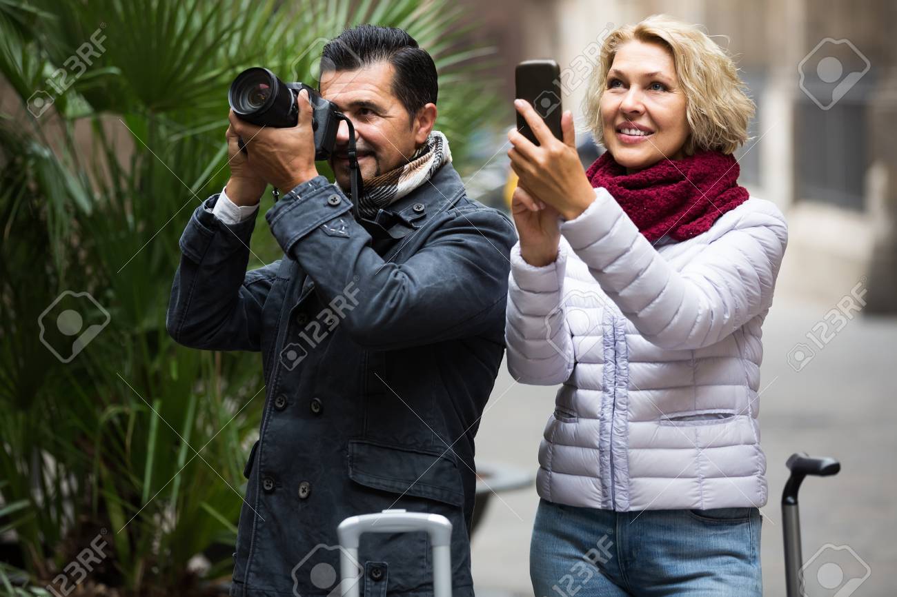 荷物 カメラとスマート フォンを歩くアメリカ熟女カップル の写真素材 画像素材 Image