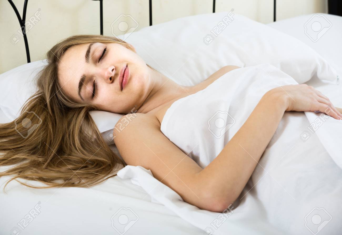 Young woman relaxed in bed, eyes gently closed, peaceful dreamy expression under light sheet