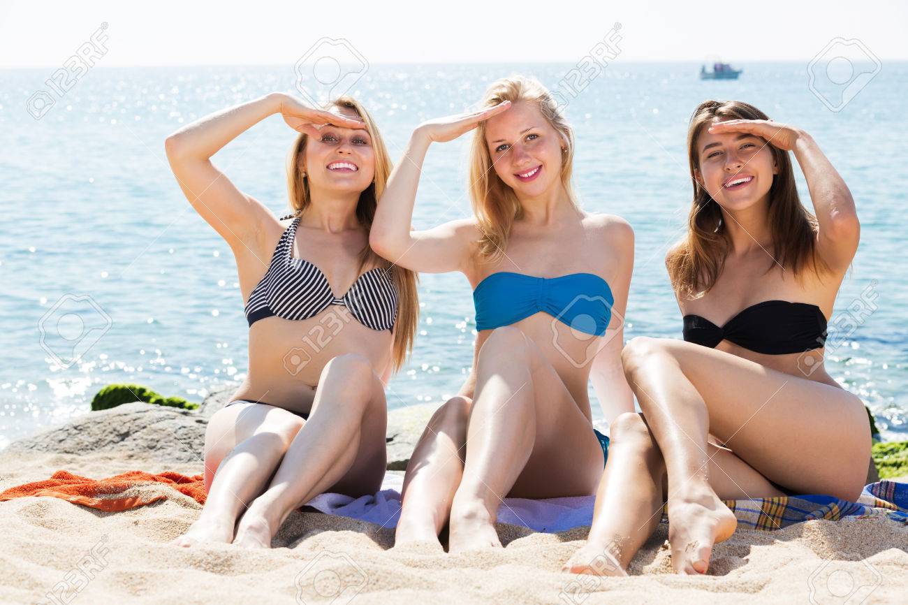 60123765-tres-chicas-j%C3%B3venes-positivas-que-llevan-el-traje-de-ba%C3%B1o-sentados-juntos-en-la-playa-y-sonriente.jpg