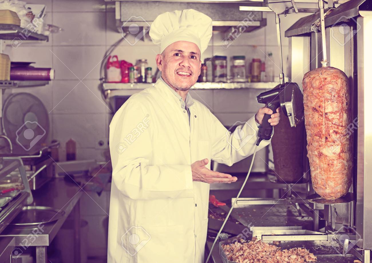 Happy Mature Man Chef Wearing Uniform Cutting Meat For Kebab