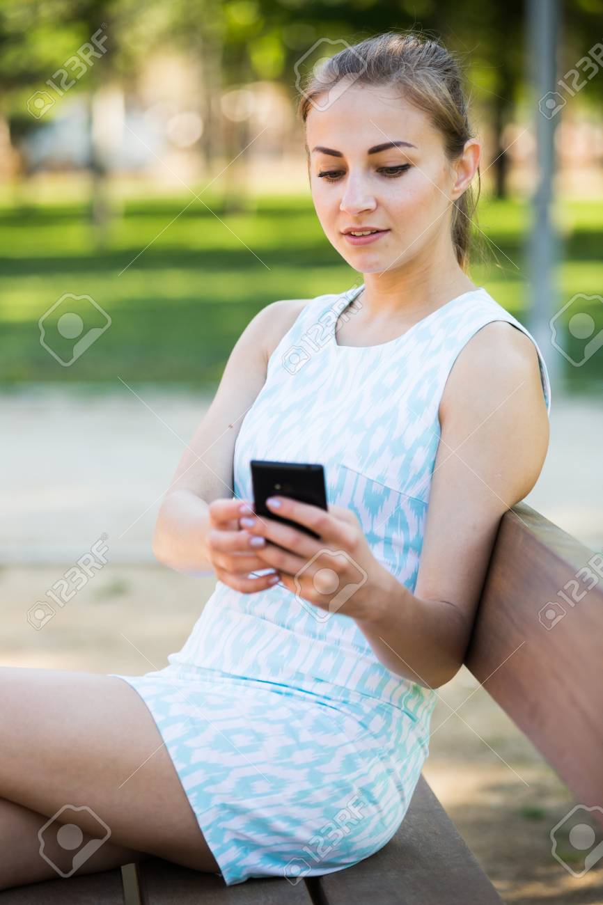 cheerful swiss girl sitting on a bench and using telephone in