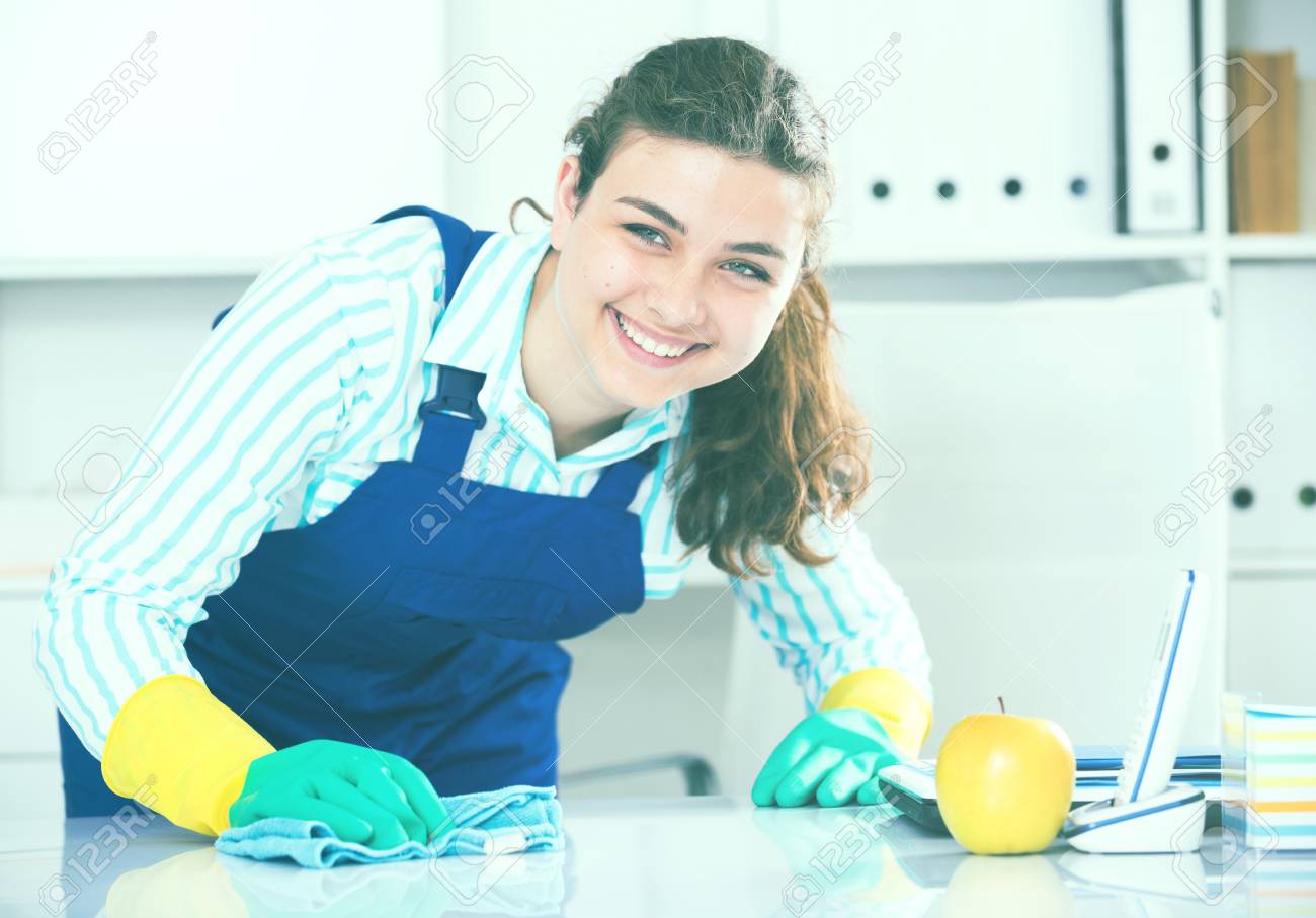 La Mujer En Uniforme Está Limpiando El Polvo Del Escritorio En La Oficina.  Fotos, retratos, imágenes y fotografía de archivo libres de derecho. Image  91948372