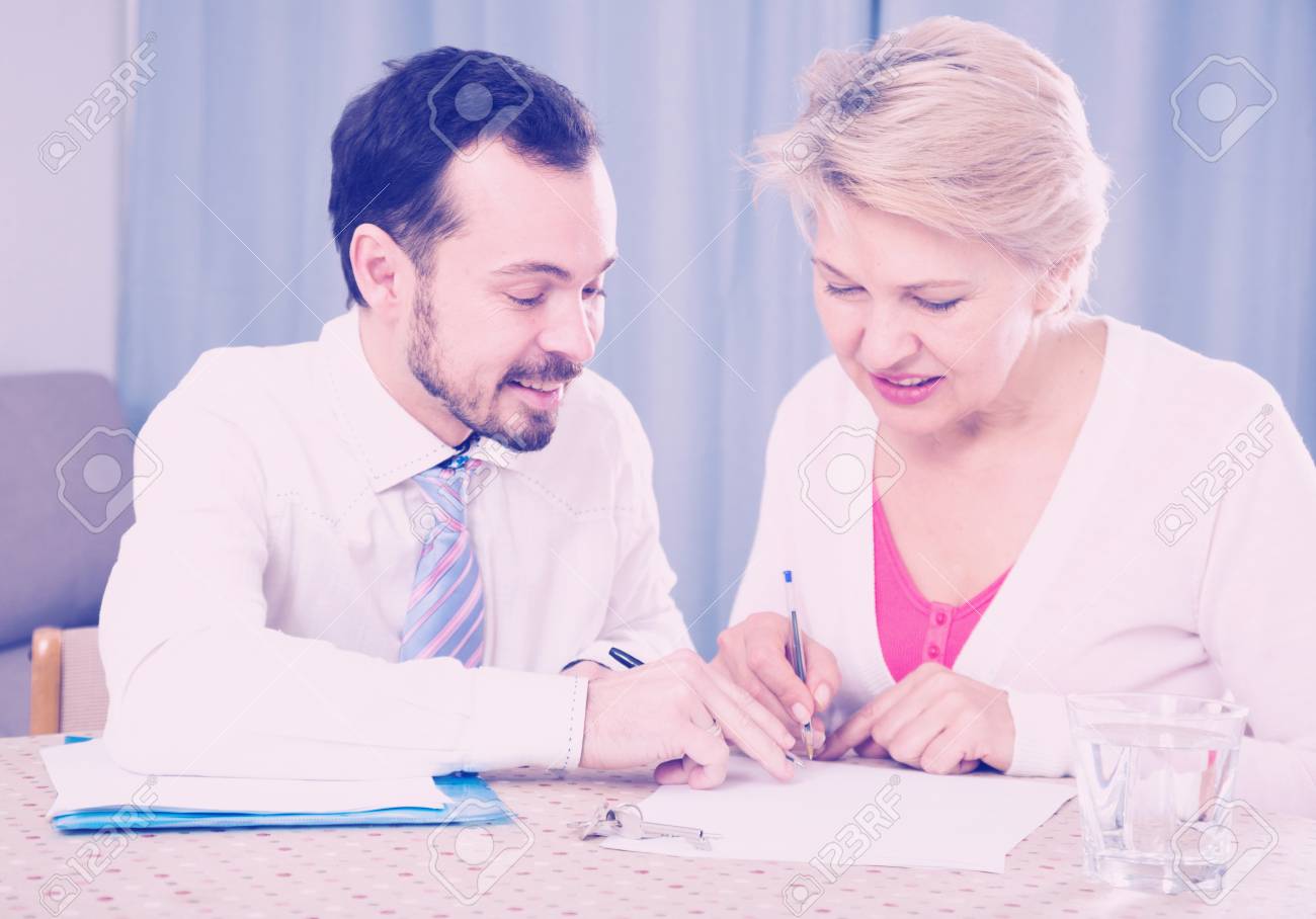 old woman signing agreement papers with social worker at home stock