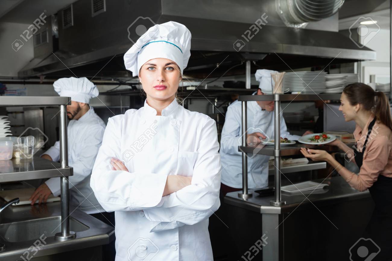 portrait of young positive smiling confident woman chef in kitchen restaurant working