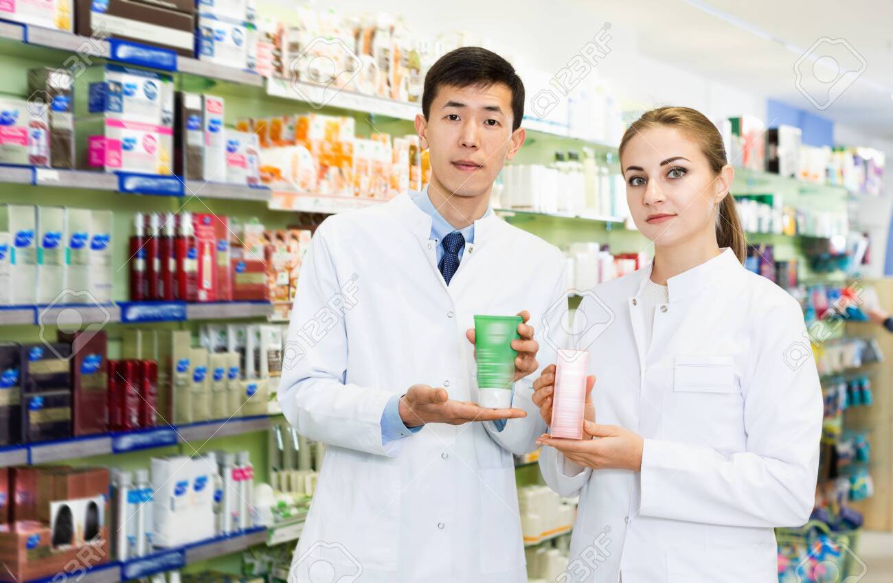 Twodiligent serious specialists are holding medicines and standing in hall of pharmacy. - 121088324 Twodiligent serious specialists are holding medicines and standing in hall of pharmacy. - 121088324