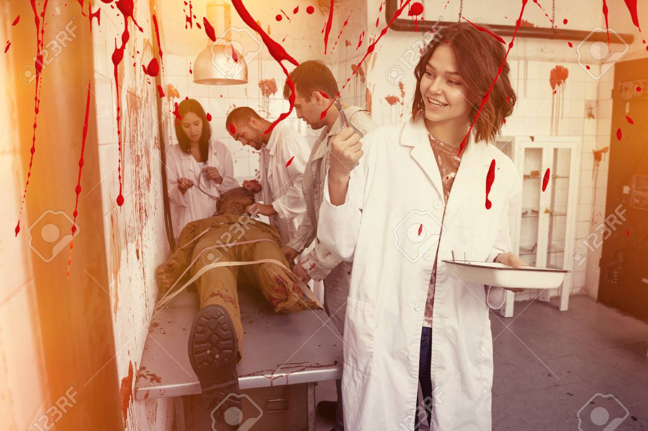 Smiling girl spending time with friends in closed space of lost room with bloody walls and zombi on table - 122507563 Smiling girl spending time with friends in closed space of lost room with bloody walls and zombi on table - 122507563