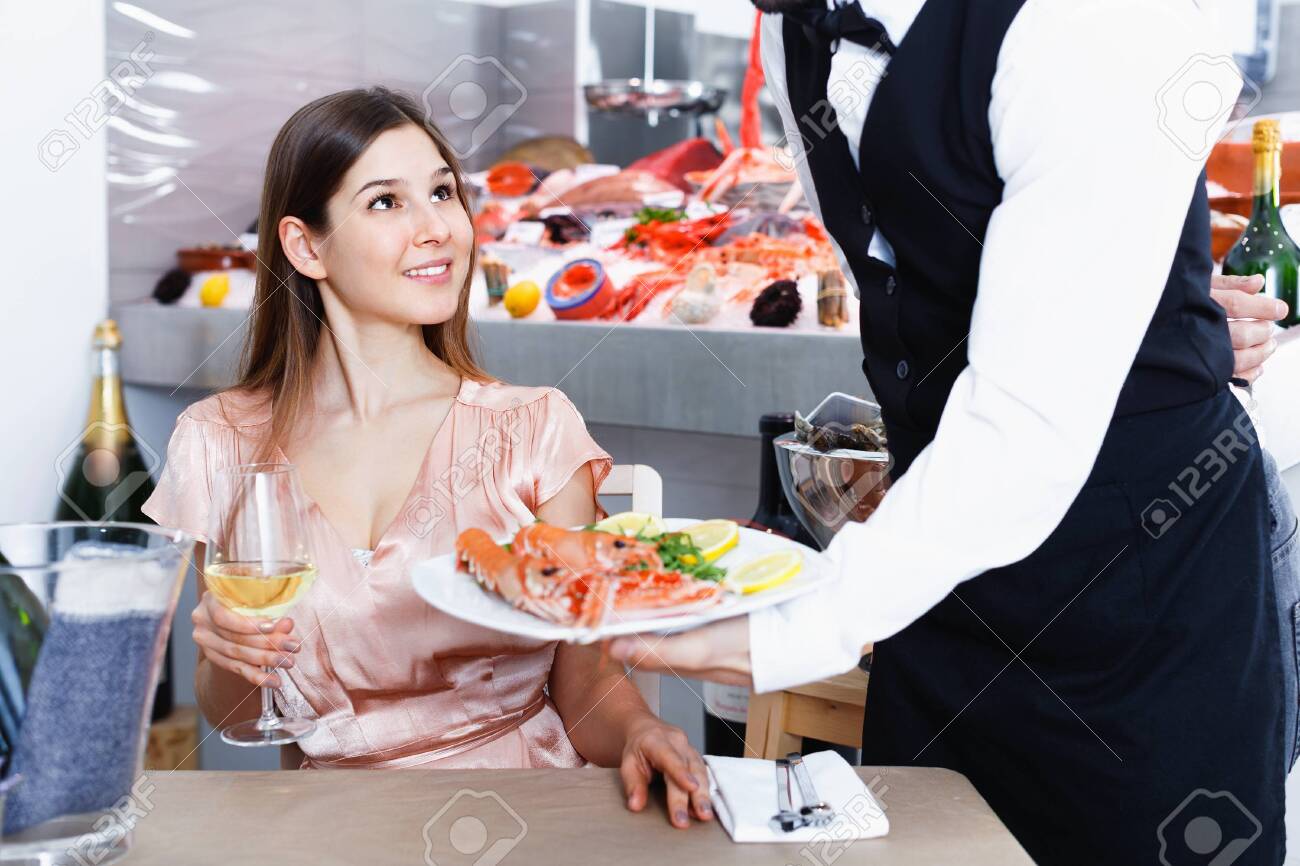 Polite waiter serving ordered seafood dishes to attractive cheerful positive girl at fish restaurant - 142538164 Polite waiter serving ordered seafood dishes to attractive cheerful positive girl at fish restaurant - 142538164