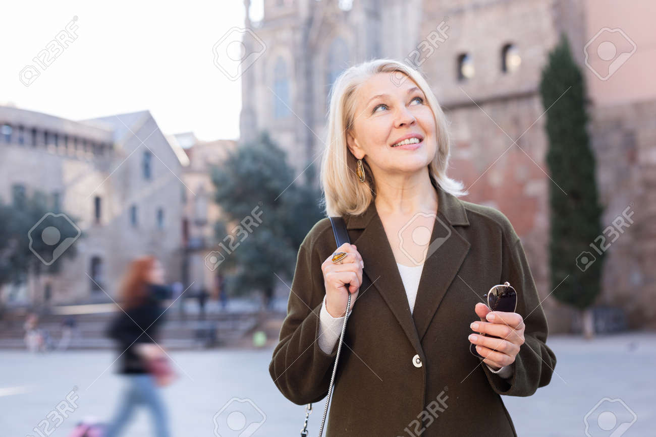 Portrait of mature cheerful woman standing on a old city street - 156255505 Portrait of mature cheerful woman standing on a old city street - 156255505