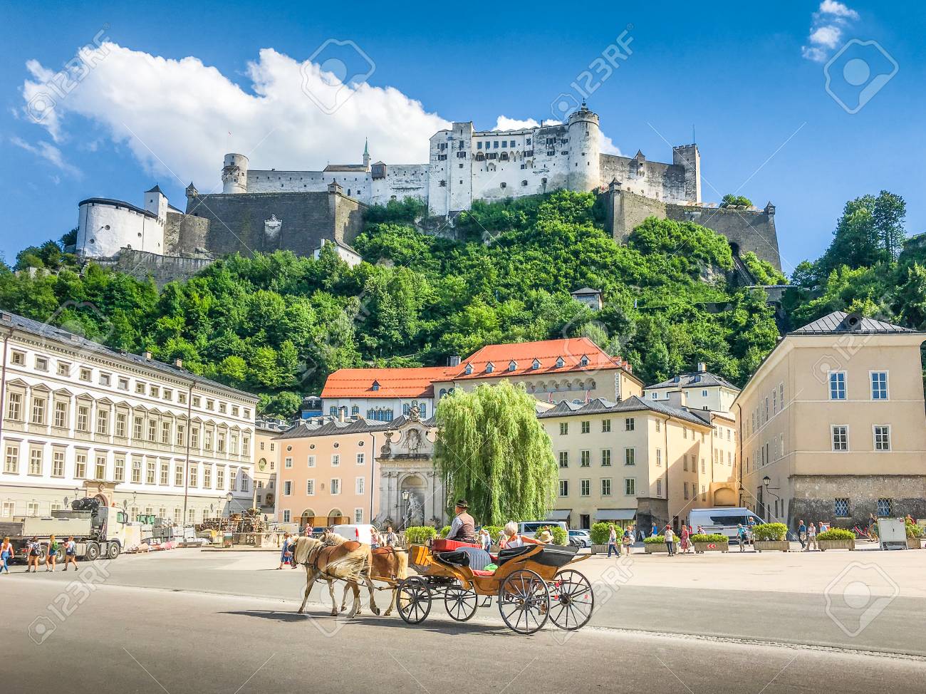 Beautiful panoramic view of the historic city of Salzburg with traditonal horse-drawn Fiaker carriage and famous Hohensalzburg Fortress on a hill on a sunny day with blue sky and clouds in summer - 100199088 Beautiful panoramic view of the historic city of Salzburg with traditonal horse-drawn Fiaker carriage and famous Hohensalzburg Fortress on a hill on a sunny day with blue sky and clouds in summer - 100199088