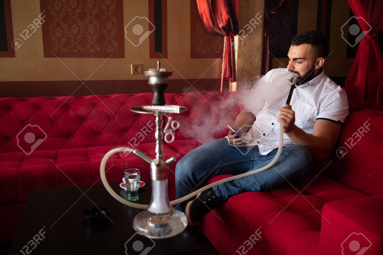 Young Man Smoking Shisha At Arabic Restaurant - Man Exhaling Smoke Inhaling  From A Hookah And Texting On Phone Stock Photo, Picture and Royalty Free  Image. Image 147954894., image size:1300x866