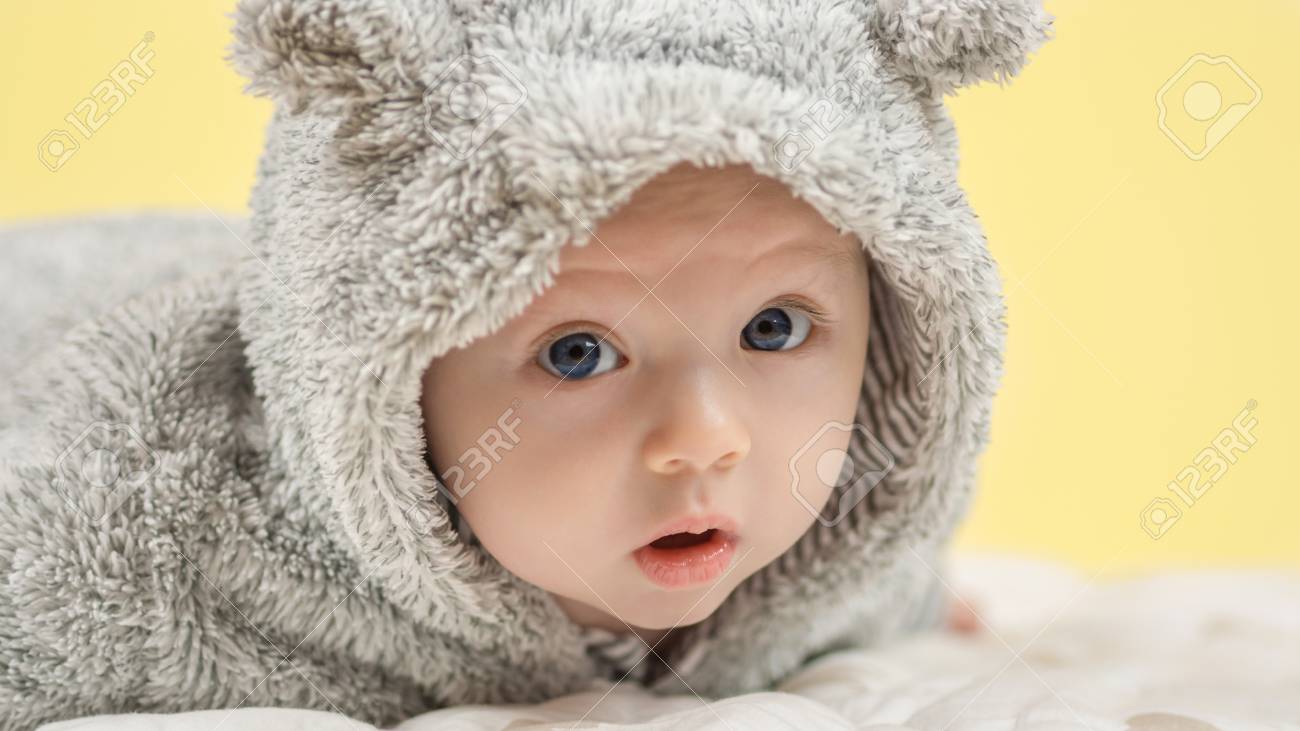 Gros Plan De Beau Bébé Heureux Aux Yeux Bleus Dans Lours Gris Comme Les Vêtements Sur Fond Jaune