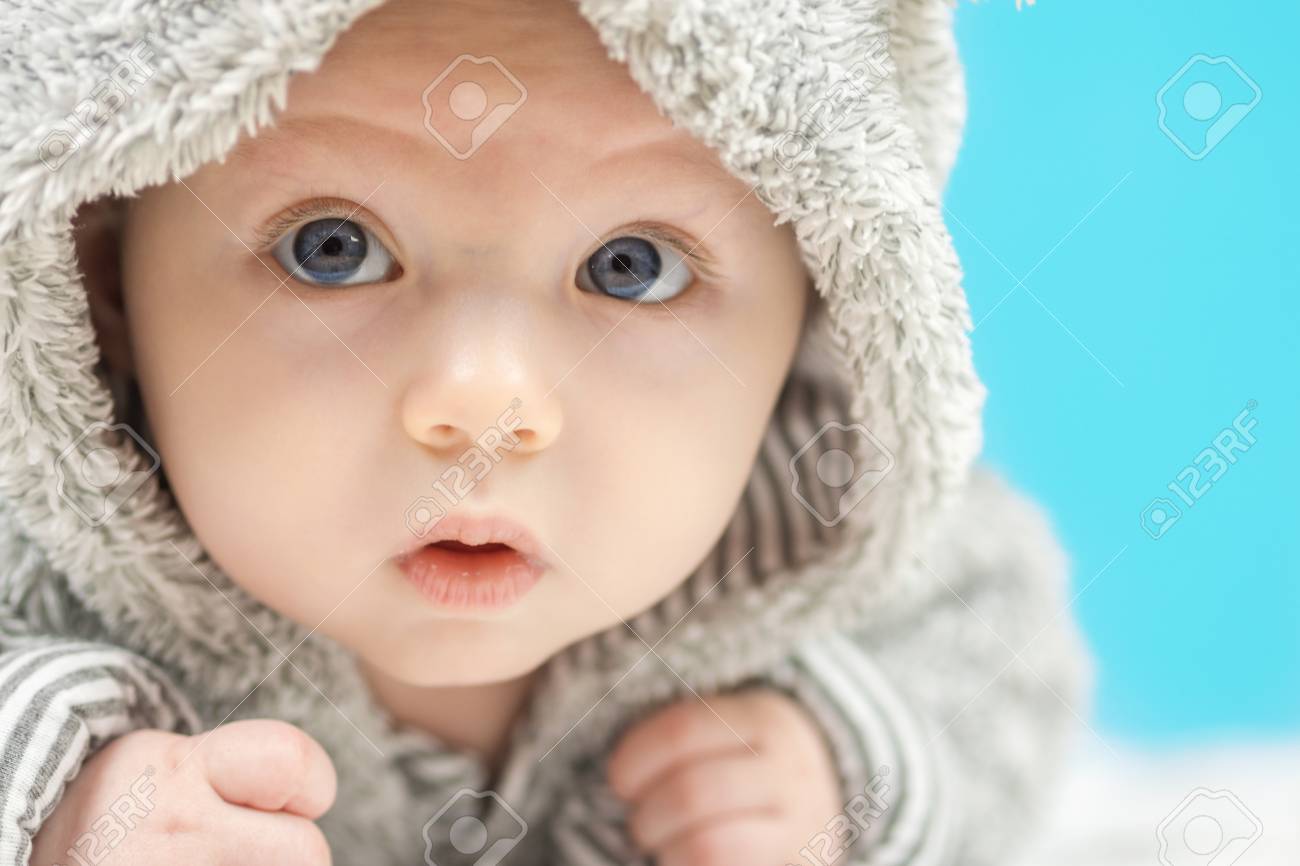 Gros Plan De Beau Bébé Heureux Aux Yeux Bleus Dans Lours Gris Comme Les Vêtements Sur Fond Bleu