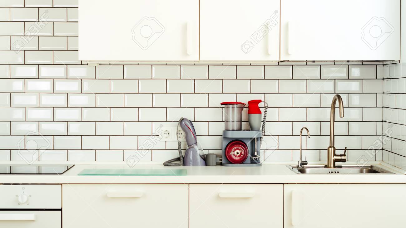 White Minimalistic Kitchen Interior And Design. Tile Wall Background.  Household Appliances - Blender, Vacuum Machine, Modern Stove, Dishwasher,  Oven, Table, Faucet Mixer. Stock Photo, Picture and Royalty Free Image.  Image 82091652., image size:1300x731
