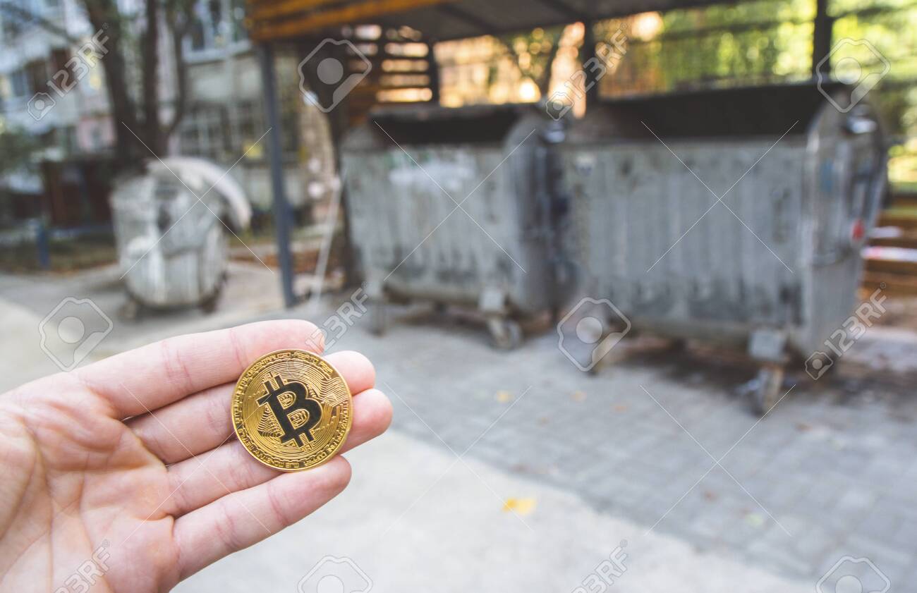 금색 비트코인을 들고 있는 손, 흐릿한 쓰레기 배경, 재활용 캔, 낮은 현대적 교환 가치 실패 개념, 화폐 가상 지불, 미래 개념.  낮은 불량 주식에 투자하는 데 사용됩니다. 로열티 무료 사진, 그림, 이미지